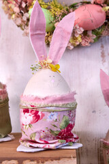 handmade Easter bunnies made of eggs with pink ears and wearing pink pants stands on a table against a green wall