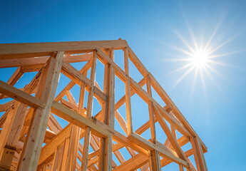 Wooden framing for a house stands tall against the vibrant blue sky, illuminated by the bright sun. Construction is in progress, showcasing craftsmanship and design
