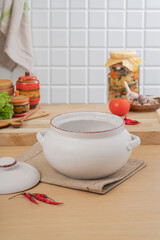 White ceramics dish with handles and lid for baking stands on kitchen table