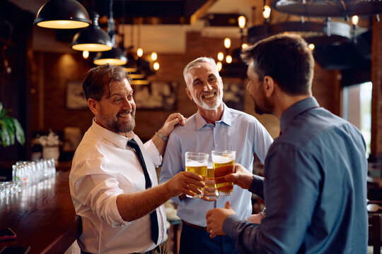 Happy male colleagues toasting while drinking beer in bar after work.