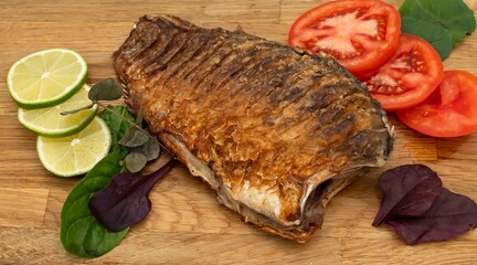 Fried crucian carp served with vegetables, lemon and herbs. Fried fish.