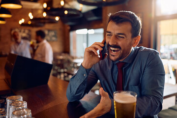 Cheerful entrepreneur talking on cell phone at bar counter.