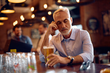 Depressed senior businessman drinking beer at bar counter.