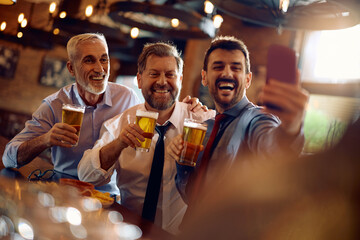 Cheerful businessmen taking selfie while drinking beer in bar.