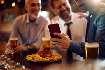 Close up of business coworkers using smart phone while drinking beer in pub.