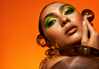 Glamorous Beauty Portrait with Green Eyeshadow and Bold Accessories on Orange Background
