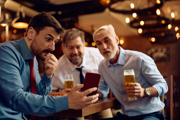 Male entrepreneur and his business coworkers watching sports match on cell phone in pub.