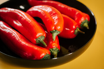 Vibrant fresh red chili peppers arranged in a black bowl on a yellow background