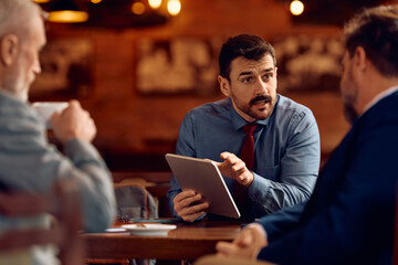 Businessman using digital tablet while talking to colleagues during meeting in cafe.