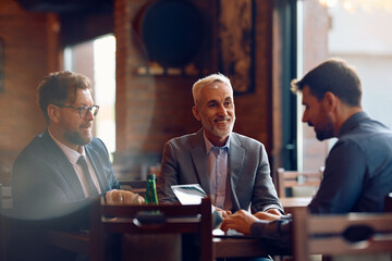 Happy senior businessman having meeting with coworkers in cafe.
