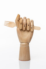 Wooden disposable fork in a wooden hand of a mannequin on a white background.