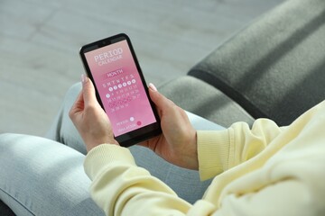 Menstruation. Woman using period calendar application on smartphone indoors, closeup
