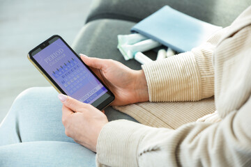 Menstruation. Woman using period calendar application on smartphone indoors, closeup