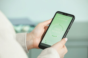 Menstruation. Woman using period calendar application on smartphone indoors, closeup