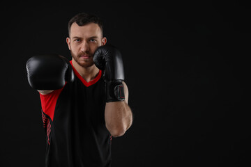 Man in boxing gloves fighting on black background, space for text