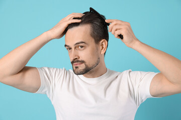 Fototapeta premium Handsome man stylish his hair with comb on light blue background