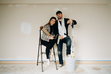 A smiling couple enjoys the process of renovating their home, working on wallpapering.