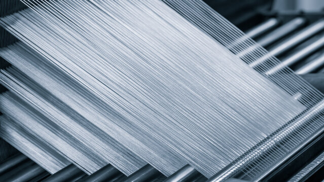 A machine is weaving a piece of fabric. The machine is made up of many parts, including a large metal piece that is connected to a hose