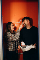 A woman cheerfully tries to paint her husband's nose, while they laugh, adding even more joy to the...