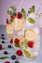 refreshing citrus and berry-infused water in elegant tall glasses with mint leaves and ice cubes against a soft pastel background, evoking a summery, vibrant, and healthy atmosphere. tasty, dessert
