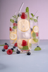 refreshing glasses of infused water with lemon, raspberry, and blueberry slices on a light...