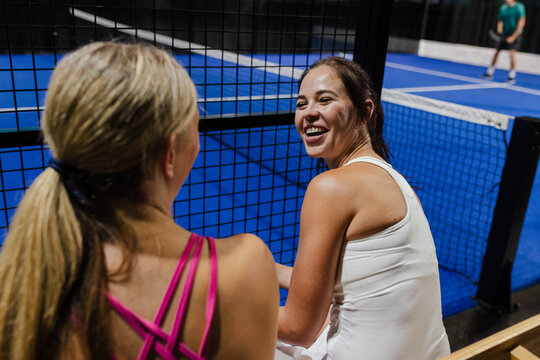 Women enjoying padel tennis match, smiling and chatting on court sidelines