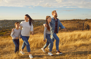 Smiling young happy family of four with two children boy and girl walking in the field together....