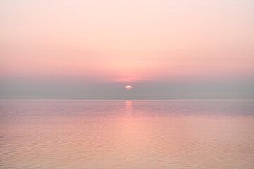 Obraz premium Pink sunset over calm water, reflecting soft light, creating a serene and peaceful atmosphere, ideal for tranquility or meditation concepts