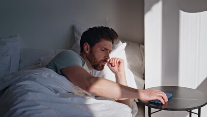 Fototapeta premium Awaking brunette looking smartphone screen bed closeup. Smiling man read message