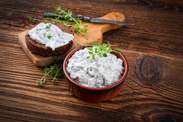 Traditional Italian obatzda with camembert and mascarpone served with garlic and spring onion on a German pumpernickel bread slice as close-up on a wooden cutting board