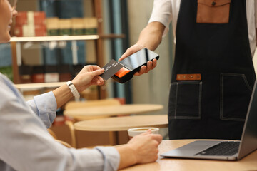Woman paying with credit card via terminal at wooden table in cafe, closeup