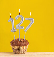 Chocolate cupcake with number 127 candle - Birthday on a yellow background