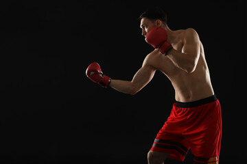 Man in boxing gloves fighting on black background, space for text
