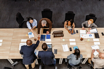 A White elder man and a Black bald man shake hands during a business meeting in a modern office,...