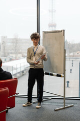 A White young man presenting during an internship meeting, holding a document in front of a flip...