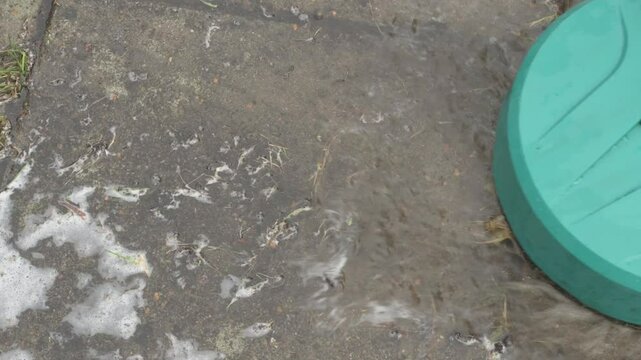 round high-pressure washer spraying foaming water on cement tiles overgrown with grass and dirt