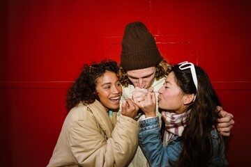 Two women smile while clinging with their pinkies to the pinky of their friend, who leans his lips...