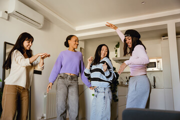 A multinational group of young women dancing and having fun together in a modern living room, they...