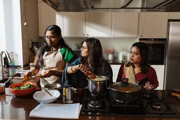 Three South Asian women are cooking together in modern kitchen, preparing a traditional homemade...