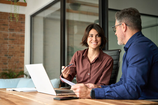 Two happy executives working on laptop discussing financial documents at meeting. Professionals team talking planning project at work. Attorney or bank manager consulting client investor in office.