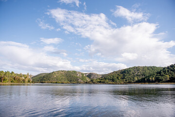 Obraz premium Visovac lake reflecting the cloudy sky with its calm waters surrounded by lush vegetation and hills, a beautiful landscape in Krka national park, Croatia, during a sunny day