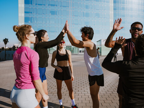 Group of six athletes standing and cheering while giving each other high fives, outdoors, after sports