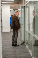 Fototapeta premium Side view of male employee standing and smiling while opening office door, in hallway, during retirement