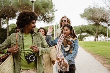 A woman walks and holds her dog while waving her hand at the back of a friend walking in front of her, on the street during a walk
