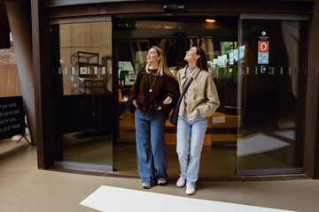 Fototapeta premium A woman walks and smiles while looking up and holding the arm of a friend walking next to her, during a trip