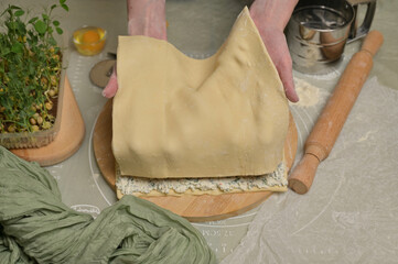 Woman's hands holding a sheet of dough. Rolling pin, cutter, eggs, green towel, microgreens sprouts on kitchen table. Home cooking baking puffs