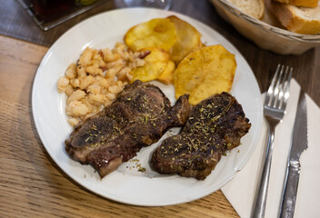 Grilled beef with spices and herbs with potatoes and beans on a white plate. Meat dish according to a traditional Spanish recipe