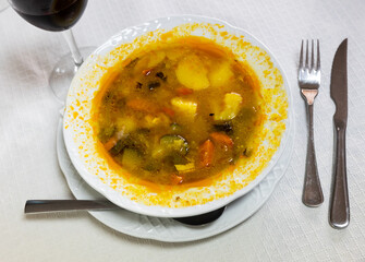Plate is filled with hot fatty soup of vegetables and chicken fillet. Glass of red wine is served...