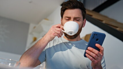 Morning man browsing smartphone at kitchen closeup. Guy drinking aromatic coffee