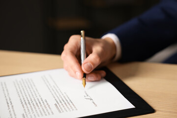 Man putting signature on document at wooden table, closeup